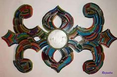 a decorative wall hanging made out of multicolored glass and metal strips with a circular mirror in the center