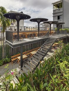 an outdoor dining area with tables and benches on the roof deck, surrounded by tropical vegetation