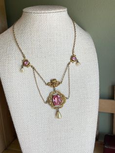 A great example of Art Nouveau jewelry 1880-1915. Gold Filled.  This choker features an Art Nouveau design with pink faceted glass and glass coated pearls.  The central drop has a large cushion shaped faceted pink glass bezel set.  Above is a goddess with flowing hair.  The drop measures 2.25" from top to bottom.  There are decorative pink glass set links with glass coated pearls.  Barrel clasp in working order. The piece overall is in very good.  Please note some loss to the coating on the round pearls.  The length is 14.25".  These pieces were meant to be worn tight to the neckline.  Possible to add some extra chain at the back to enlarge.  The color of the faceted glass is a beautiful pink -mimics a pink sapphire.  Rarely do I get such a fine example in hand.  14 day return policy. Decorative Pink Jewelry Gift, Elegant Pink Cabochon Necklace, Antique Pink Jewelry For Formal Occasions, Pink Oval Victorian Jewelry, Victorian Pink Jewelry For Formal Occasions, Vintage Pink Oval Necklace, Formal Pink Cabochon Necklace, Formal Antique Pink Jewelry, Antique Pink Necklaces For Wedding