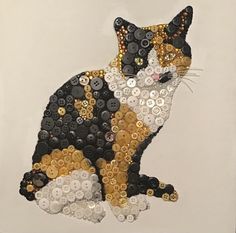 a cat made out of buttons sitting on top of a white sheet with gold and black sequins