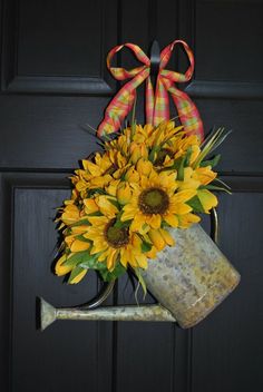 a metal watering can with sunflowers hanging from it's side on a door