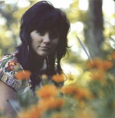 a woman with long black hair standing in flowers