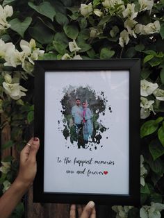 a person holding up a framed photo with flowers in the background