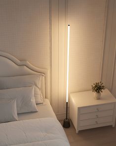 a white bed sitting next to a night stand with a lamp on top of it