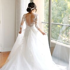 a woman in a wedding dress looking out the window with her back to the camera