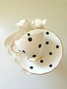 a polka dot tea cup and saucer with two birds on the side, sitting on top of each other