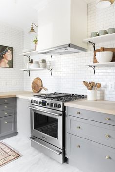 a kitchen with gray cabinets and white subway backsplash, stainless steel range hood