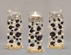 three glass vases with lights in them on a white surface, one is filled with black balls