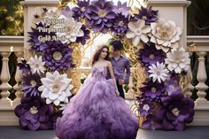 two people standing in front of a purple and white backdrop with flowers on the wall