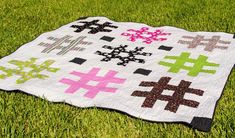 a quilt is laying on the grass in front of some green grass with pink, black and white crosses