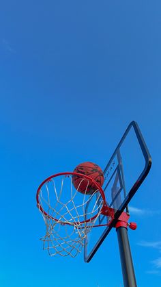 a basketball going through the rim of a basketball hoop on a clear blue sky day