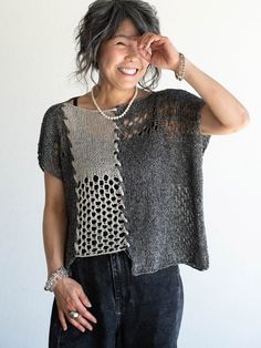 a woman standing in front of a white wall wearing a black and grey top with holes on it