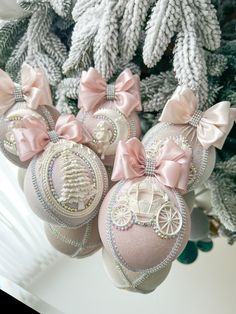 some ornaments are hanging from a tree with pink bows on it's head and in the shape of a baby carriage