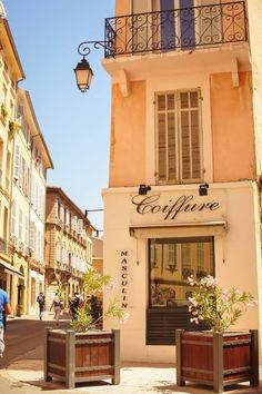 the front entrance to a coffee shop with potted plants on the sidewalk and people walking by