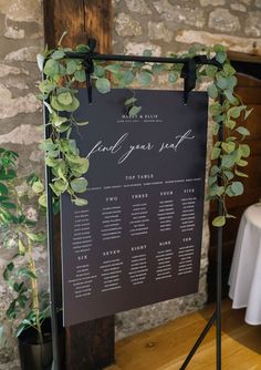 a sign with greenery on it sitting in front of a stone wall and table