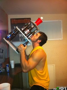 a man in yellow shirt holding up a machine to his face with two cups on top of it