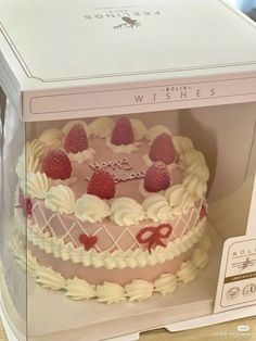 a pink cake with white frosting and strawberries on top in a clear box