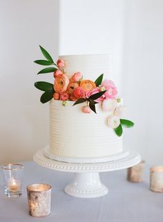 a white wedding cake with flowers on top and candles in the background, sitting on a table