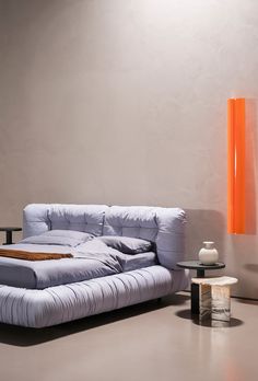 a modern day bed with an orange lamp next to it