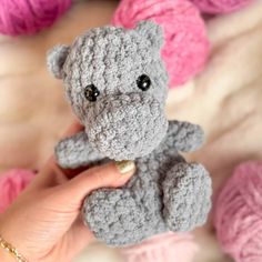 a hand holding a small gray crocheted teddy bear in front of balls of yarn