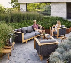 two people sitting on couches in the middle of an outdoor area with potted plants