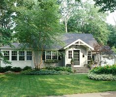 a house that is in the middle of some grass and trees with bushes around it