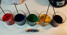 four glasses with different colored liquids in them on a table next to a blender