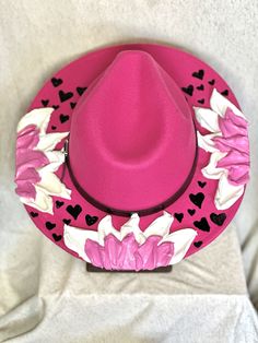 This one of a kind, hand painted, textured floral fedora is the perfect walking art piece. Each hat is uniquely crafted and perfect for any occasion.  This pink fedora is crafted with pink and white flowers with black accent hearts.  These island treasures are shipped straight to you from the Hawaiian island of Oahu. (Hats are water resistant. Keep out of heavy rain. Spot clean only) Pink Bohemian Fedora For Spring, Handmade Pink Fedora With Flat Brim, Pink Fedora Felt Hat For Kentucky Derby, Western Style Pink Felt Hat For Spring, Pink Fedora For Kentucky Derby, Pink Western Felt Hat For Spring, Handmade Pink Fedora For Spring, Pink Fedora For Country Events, Pink Western Fedora For Spring