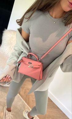 a woman holding a pink handbag in her right hand and looking at the camera