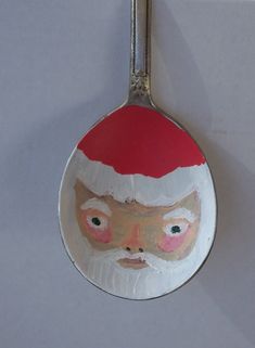 a spoon with a santa claus face painted on it's side, hanging from a wall