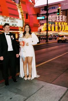 a man and woman standing next to each other in front of a neon sign at night