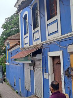 a man is walking down the street in front of a blue building with shutters