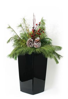 a black vase filled with pine cones and greenery