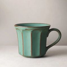 a teal colored mug sitting on top of a white table