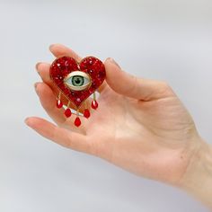 a hand holding a red heart shaped brooch with an eye on it