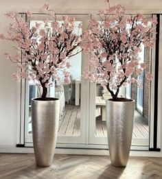 two tall vases with pink flowers in them on a wooden floor next to an open door