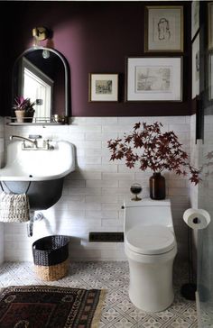 a white toilet sitting next to a sink in a bathroom under a mirror and framed pictures on the wall