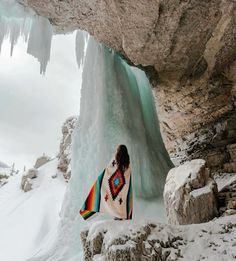 a woman standing in front of an ice cave with a colorful blanket on her shoulders