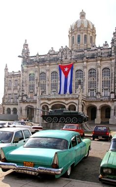 old cars are parked in front of a large building with a flag on it's side