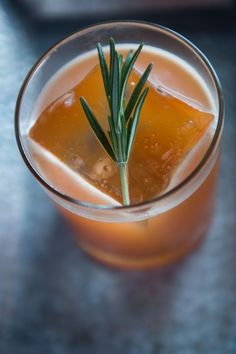 a close up of a drink in a glass with a rosemary sprig on top