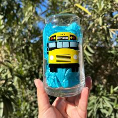 a hand holding up a glass with blue tissue paper in it and a yellow school bus on the side