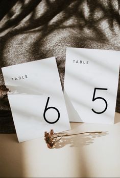 two table numbers are placed next to each other on a piece of paper with dried flowers