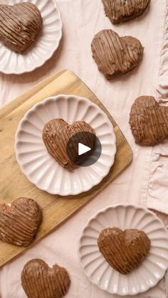 heart shaped chocolates are on paper plates next to a wooden cutting board and pink tablecloth