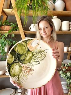 a woman holding up a plate with vegetables painted on it and plants in the background