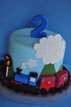 a birthday cake with a train on the front and number 2 on the back, sitting on a table