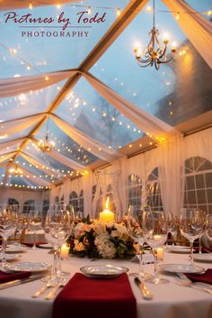 a table set up for a formal dinner under a tent with lights on the ceiling