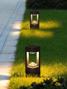 two lawn lights sitting on the side of a sidewalk next to green grass and bushes