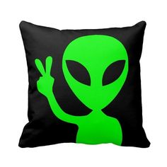 a green alien pillow sitting on top of a black pillow cover with the word peace sign in