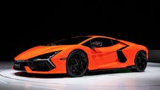 an orange sports car on display in a dark room with white floor and black walls