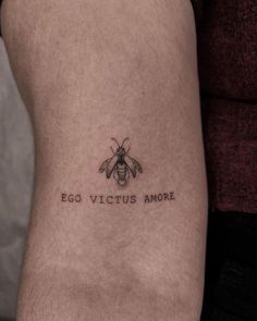 a small black and white bee tattoo on the right arm with words written below it